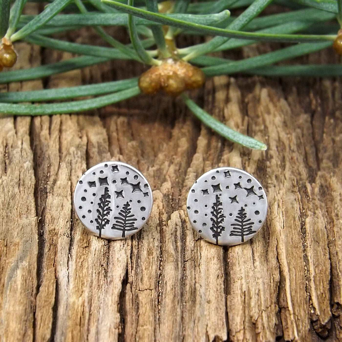 Front view of a pair of sterling silver earrings hand-stamped with a starry night forest design.
