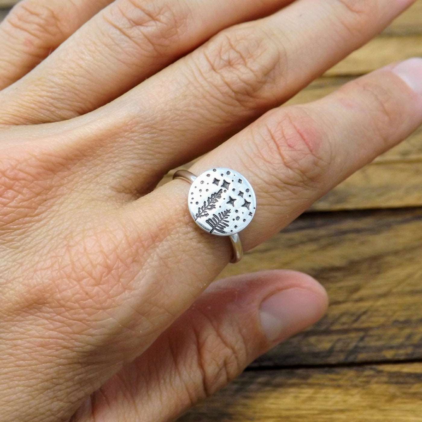 Sterling silver ring hand-stamped with a starry night forest design, worn on a finger.