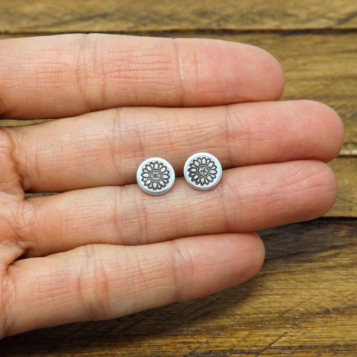 Size reference view of sterling silver stud earrings hand-stamped with sunflower design.