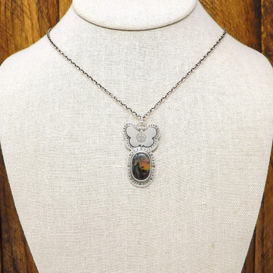 Bust view of a sterling silver dendritic agate gemstone necklace adorned with a butterfly stamped with the Jenn's Zen Creations logo. A hand-stamped design borders the pendant.