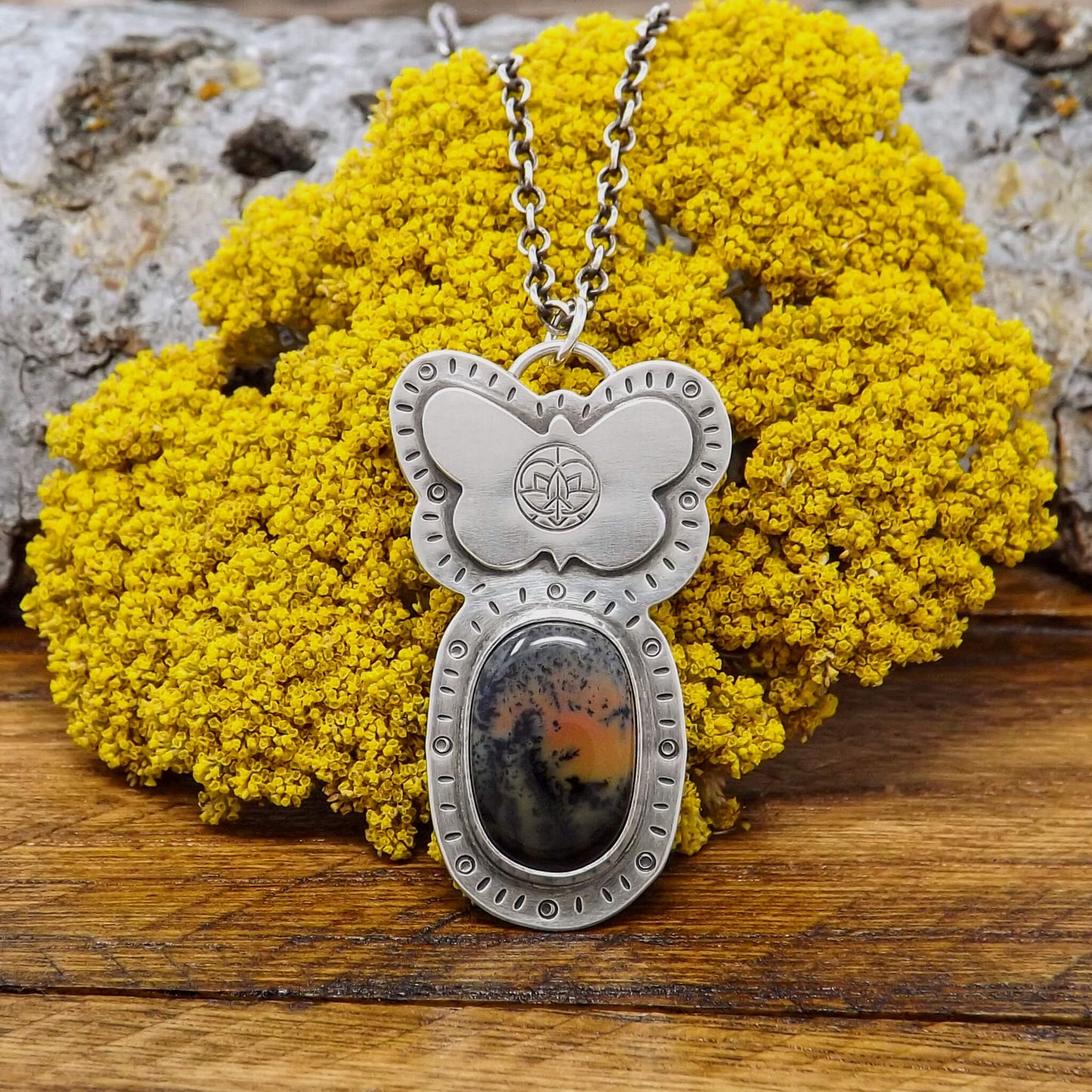 Front view of a sterling silver dendritic agate gemstone necklace adorned with a butterfly stamped with the Jenn's Zen Creations logo. A hand-stamped design borders the pendant.