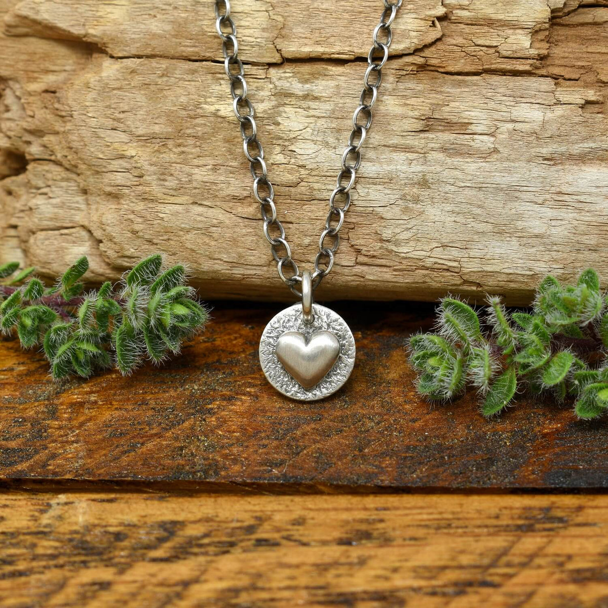 Hand-fabricated sterling silver heart necklace with a smooth dimensional heart on a hand-stamped textured disc.