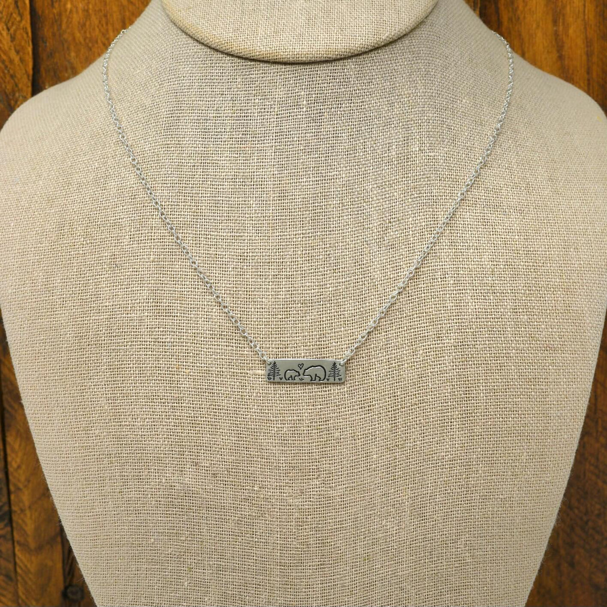 Sterling silver mama bear and baby bear bar necklace with hand-stamped woodland scene, display on a necklace bust.