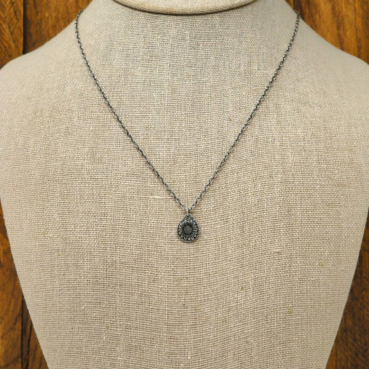 Hand-fabricated sterling silver necklace with a 3-dimensional sunflower on a hand-stamped textured teardrop shape silver disc, displayed on a necklace bust.