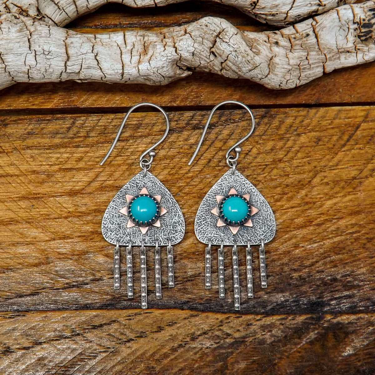 Close up front view of a pair of sterling silver dangle earrings with hubei turquoise gemstones and a copper sun design.