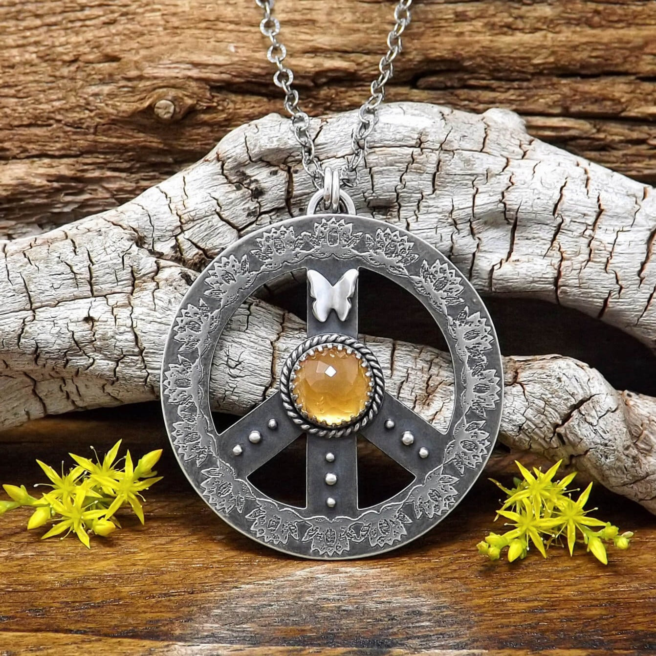Front view of a sterling silver peace sign necklace with etched lotus flowers, a butterfly, argentium silver granules and a rose cut faceted hessonite garnet gemstone.