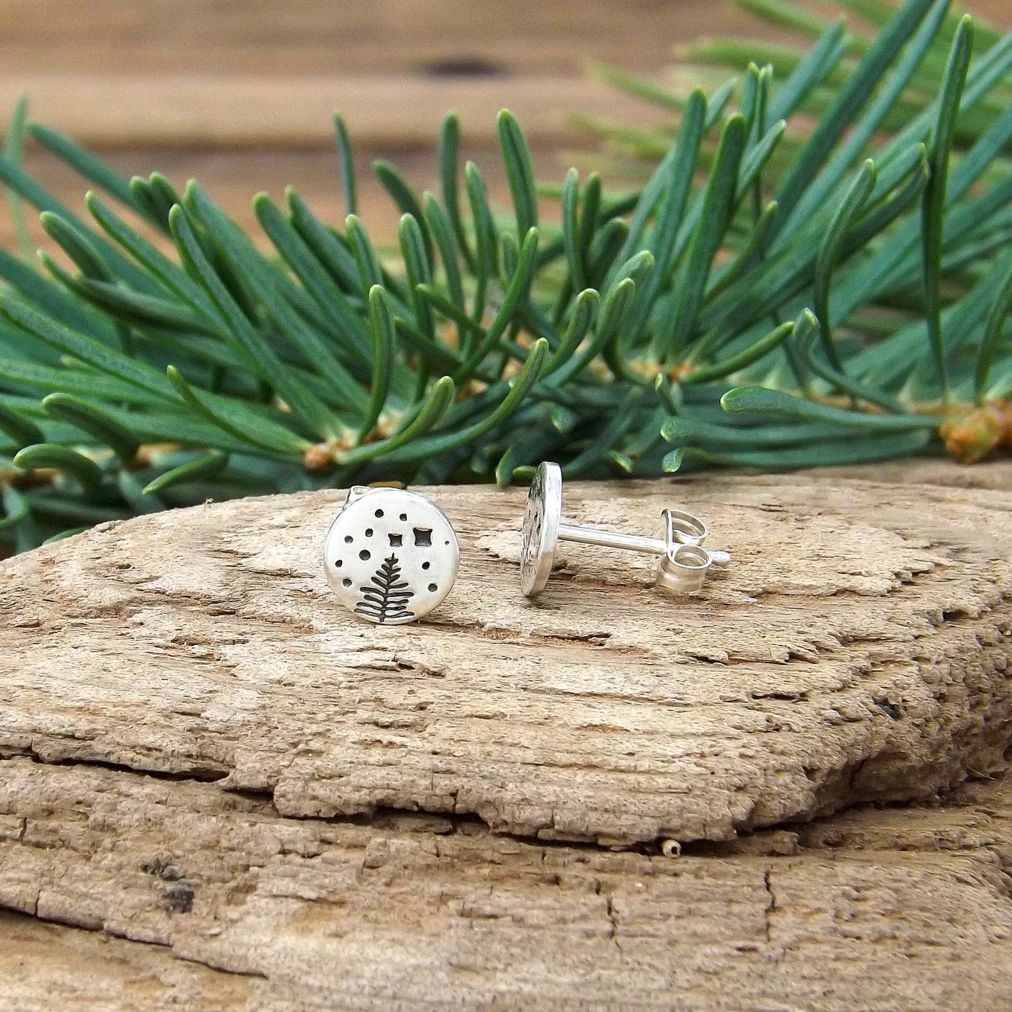 Side view of a pair of sterling silver stud earrings with a hand-stamped starry night pine tree design.