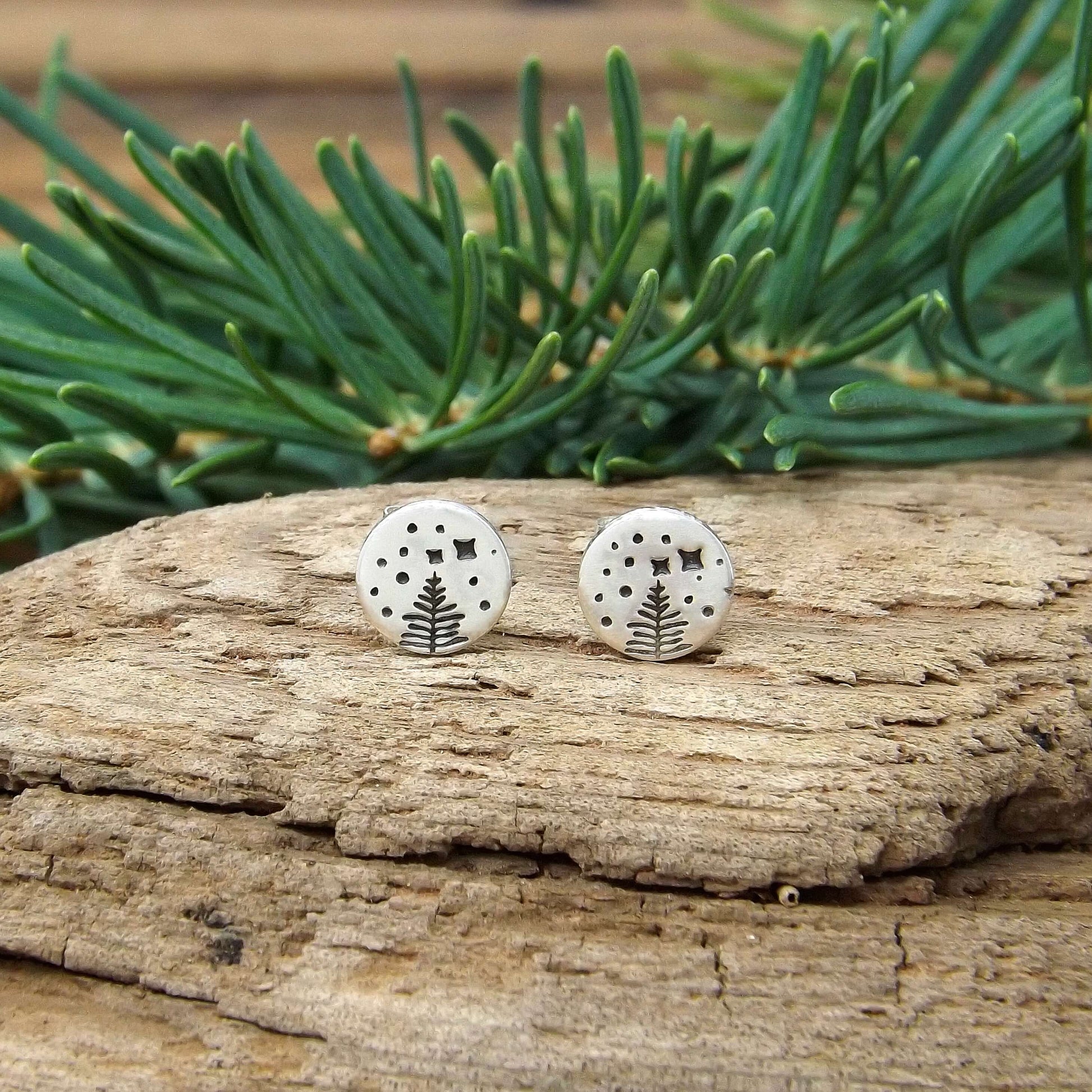 Front view of a pair of sterling silver stud earrings with a hand-stamped starry night pine tree design.