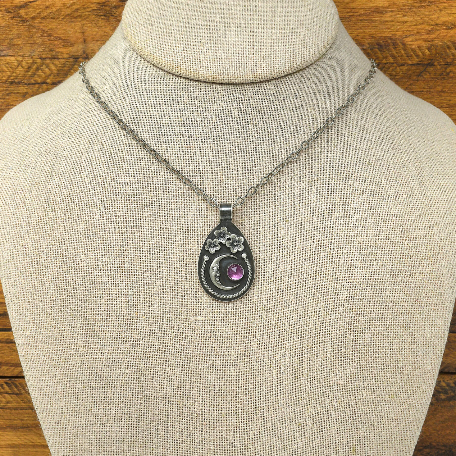 Sterling silver cherry blossom and crescent moon necklace with a rose cut faceted rhodolite garnet shown on a display bust.