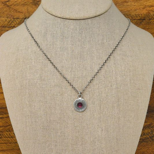 Bust view of a sterling silver sunburst necklace with a rose cut faceted rhodolite garnet gemstone.