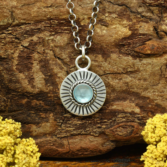Front view of a sterling silver sunburst necklace with a rose cut faceted sky blue topaz gemstone.