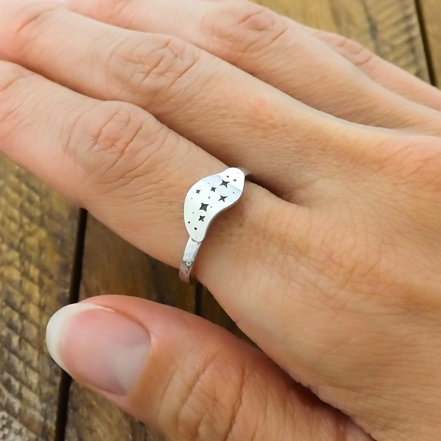 Sterling silver ring with a hand-stamped star cluster design, worn on a finger.