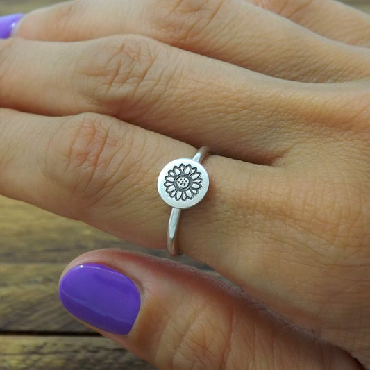 sterling silver stacking ring hand-stamped with sunflower design, worn on finger.