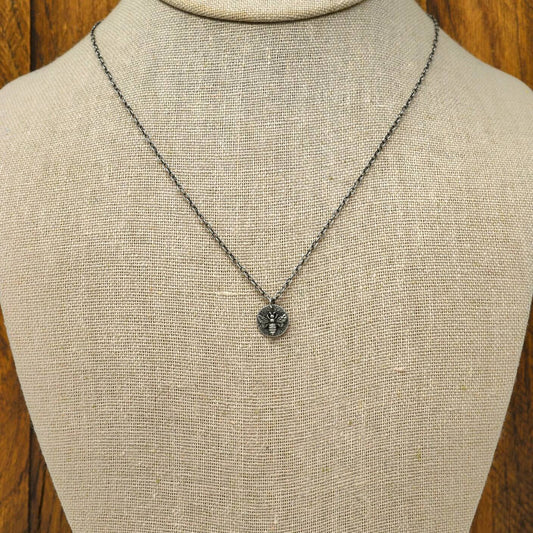 Hand-fabricated sterling silver heart necklace with a 3-dimensional bee on a hand-stamped textured disc, displayed on a necklace bust.