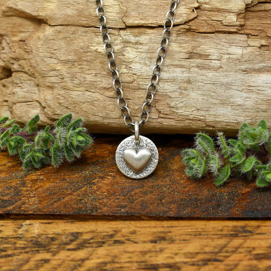 Hand-fabricated sterling silver heart necklace with a smooth dimensional heart on a hand-stamped textured disc.