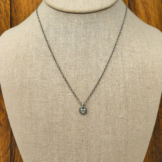 Hand-fabricated sterling silver heart necklace with a smooth dimensional heart on a hand-stamped textured disc, displayed on a necklace bust.